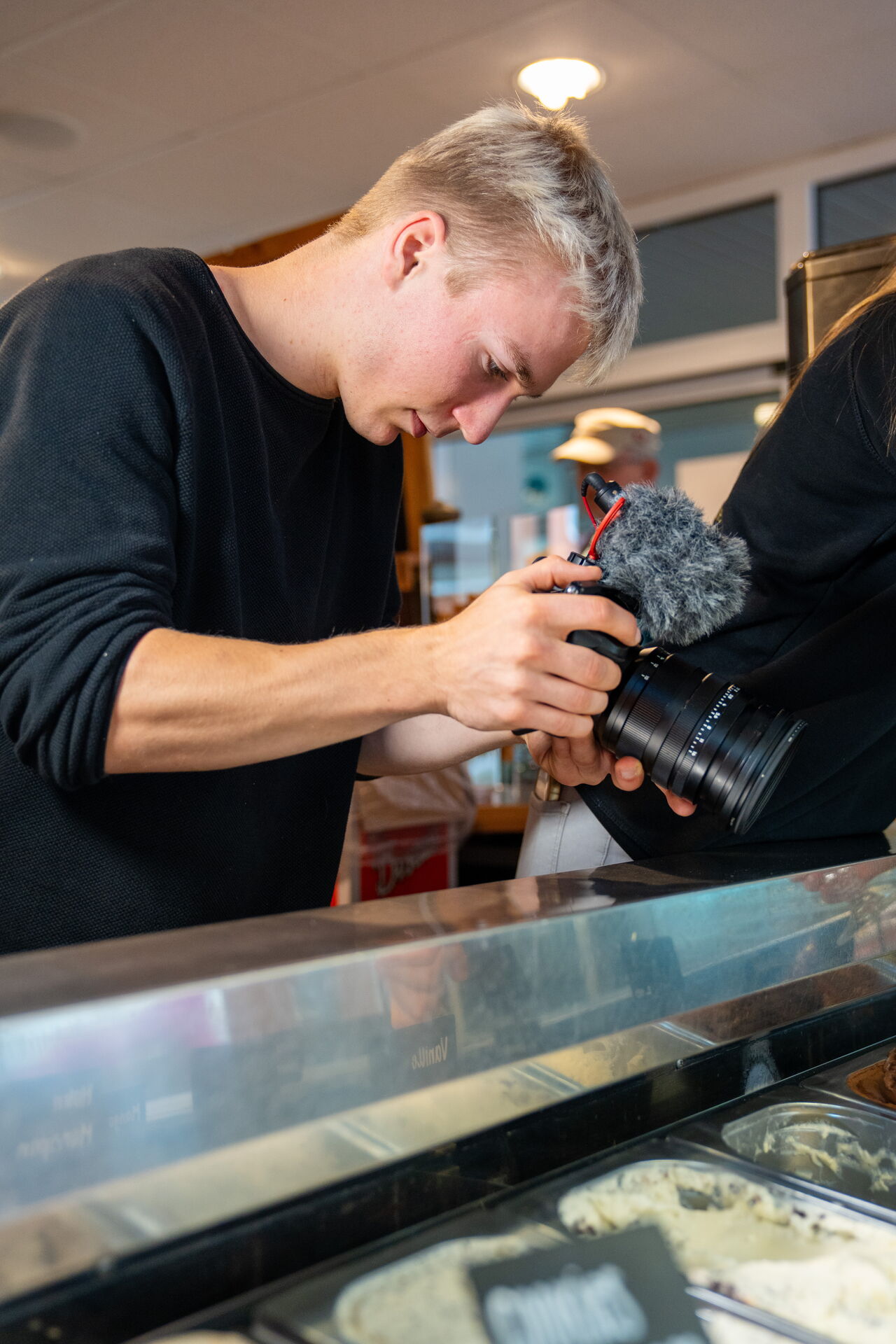 Arne Görlitz hält eine Kamera mit Windschutz am Mikrofon vor einer Glasvitrine