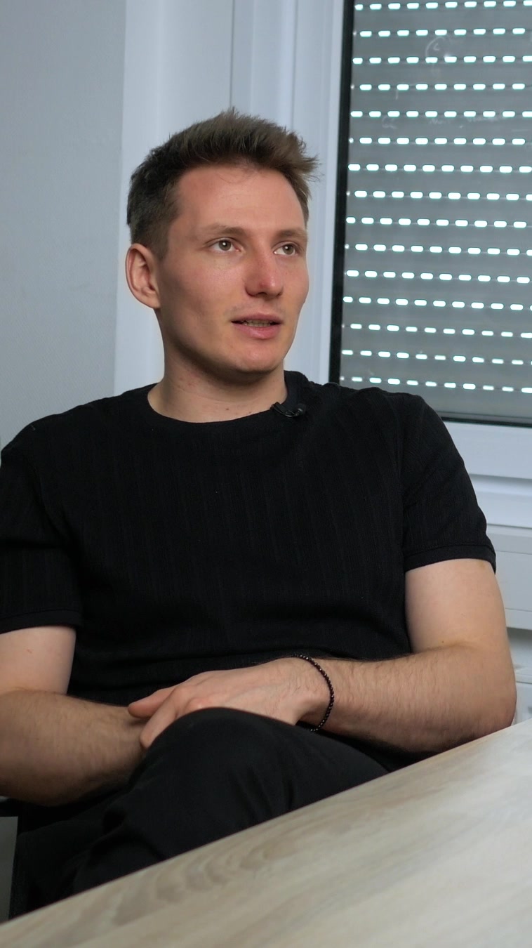 Theodor Glöer im schwarzen T-Shirt sitzt an einem Holztisch und spricht im Interview über Reichweite