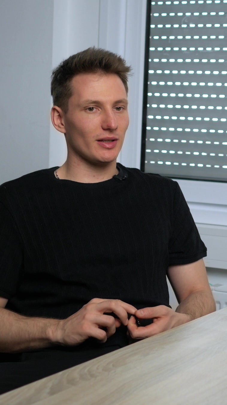 Theodor Glöer im schwarzen T-Shirt sitzt an einem Holztisch und spricht im Interview über Zielgruppen